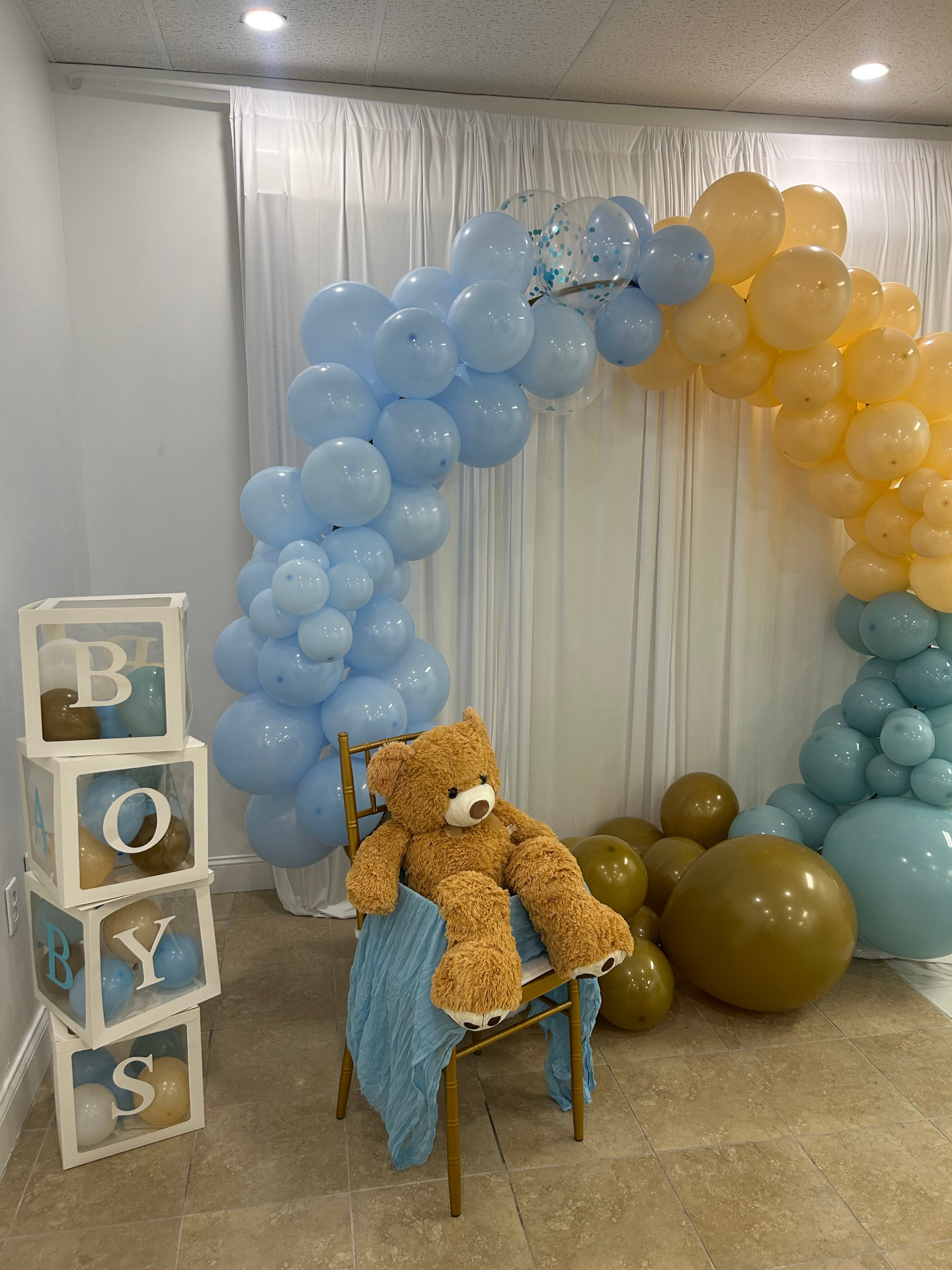 Teddy bear beneath a blue and gold balloon arch